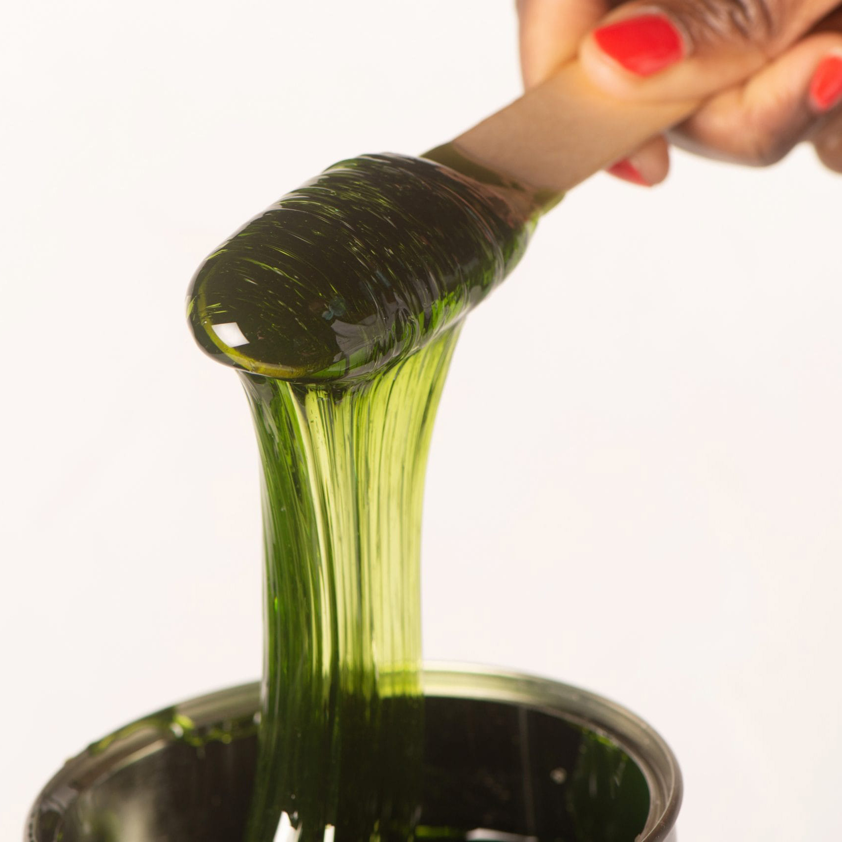 Close-up of a hand with red nails pouring a green bottle into a glass, showing the bottle neck and liquid flow.