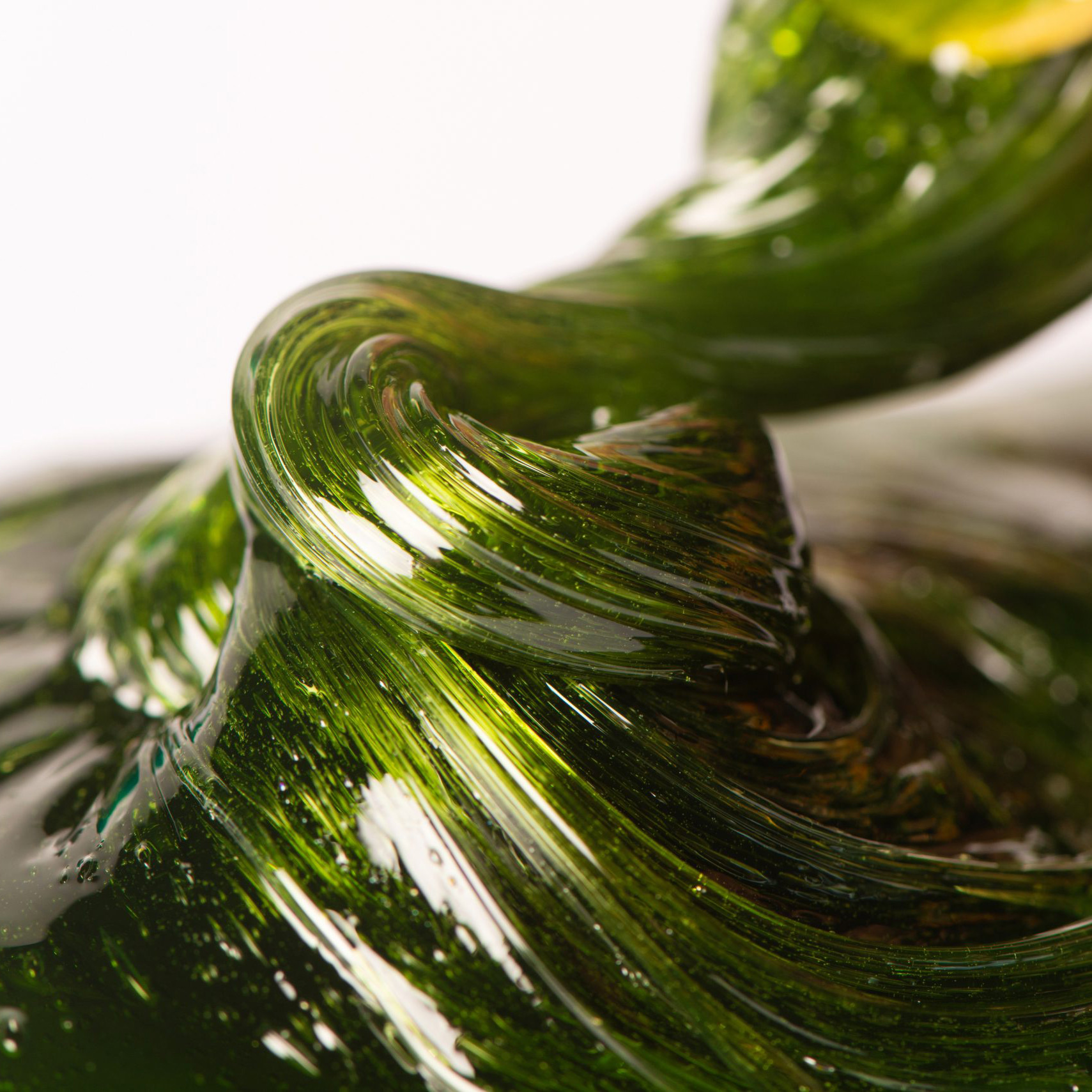 Close-up of overlapping green glass curves with bright highlights, forming a swirling abstract shape.