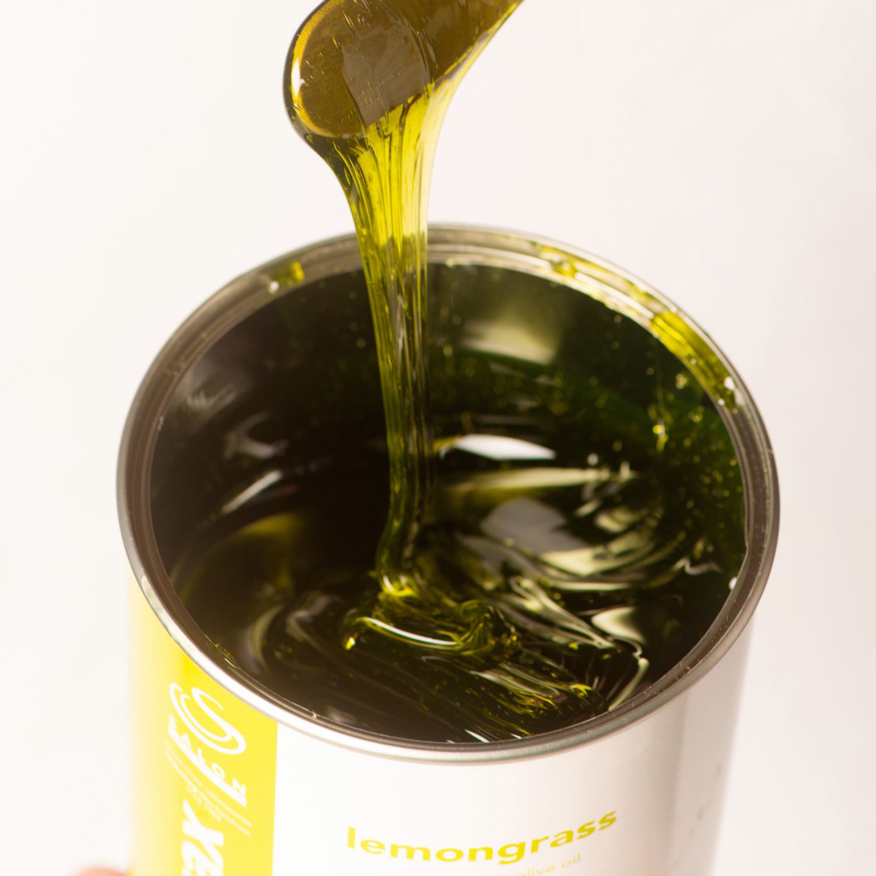 Pouring lemongrass olive oil from a bottle into a metal container.