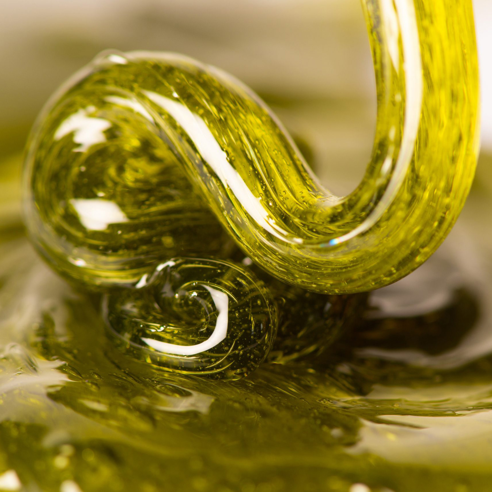 Close-up of curved, transparent yellow glass tubes submerged in a viscous yellow liquid with reflections and bubbles.