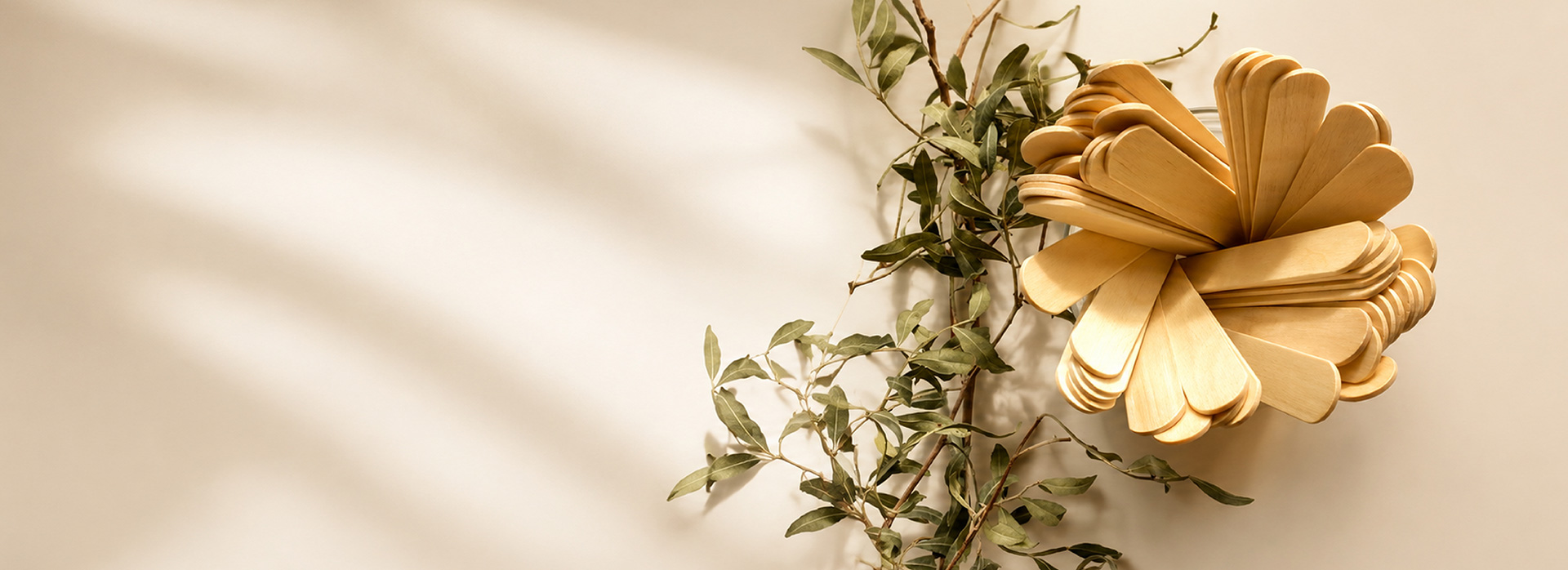 Decorative bow made from wooden spoons with green leafy branches on a beige background