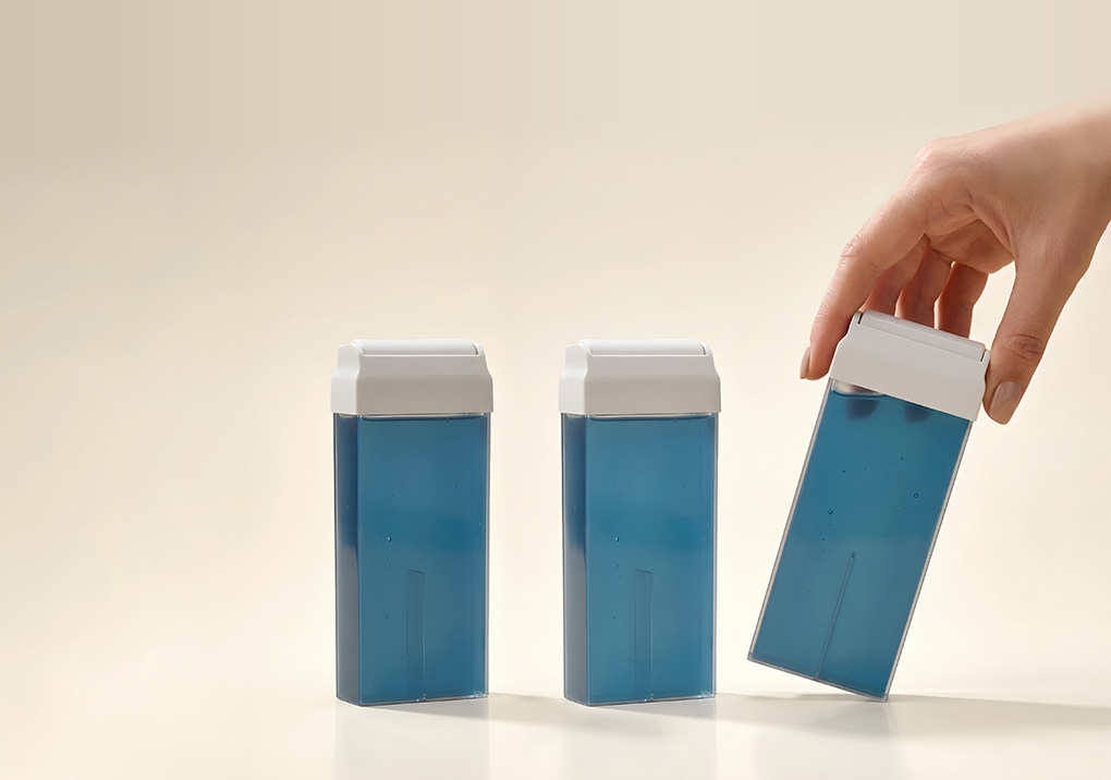 Three blue medication bottles with white caps stand on a pale surface, and a hand lifts the rightmost bottle.