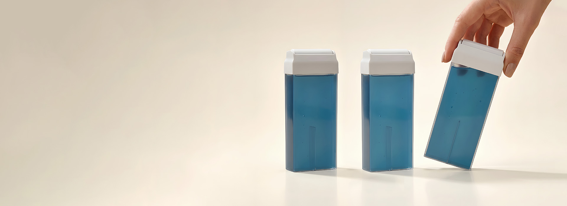 Three blue pill bottles with white caps on a pale surface, with a hand lifting one bottle from the right side.