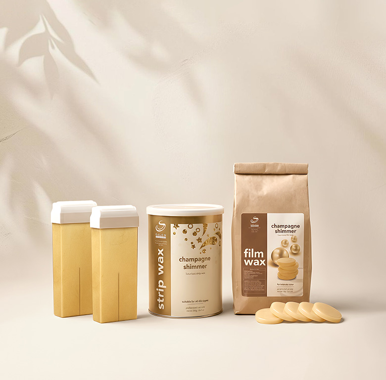 Assorted waxing products on a pale surface: two beige squeeze bottles, a champagne shimmer strip wax can, a film wax in a paper bag, and beige wax discs nearby.