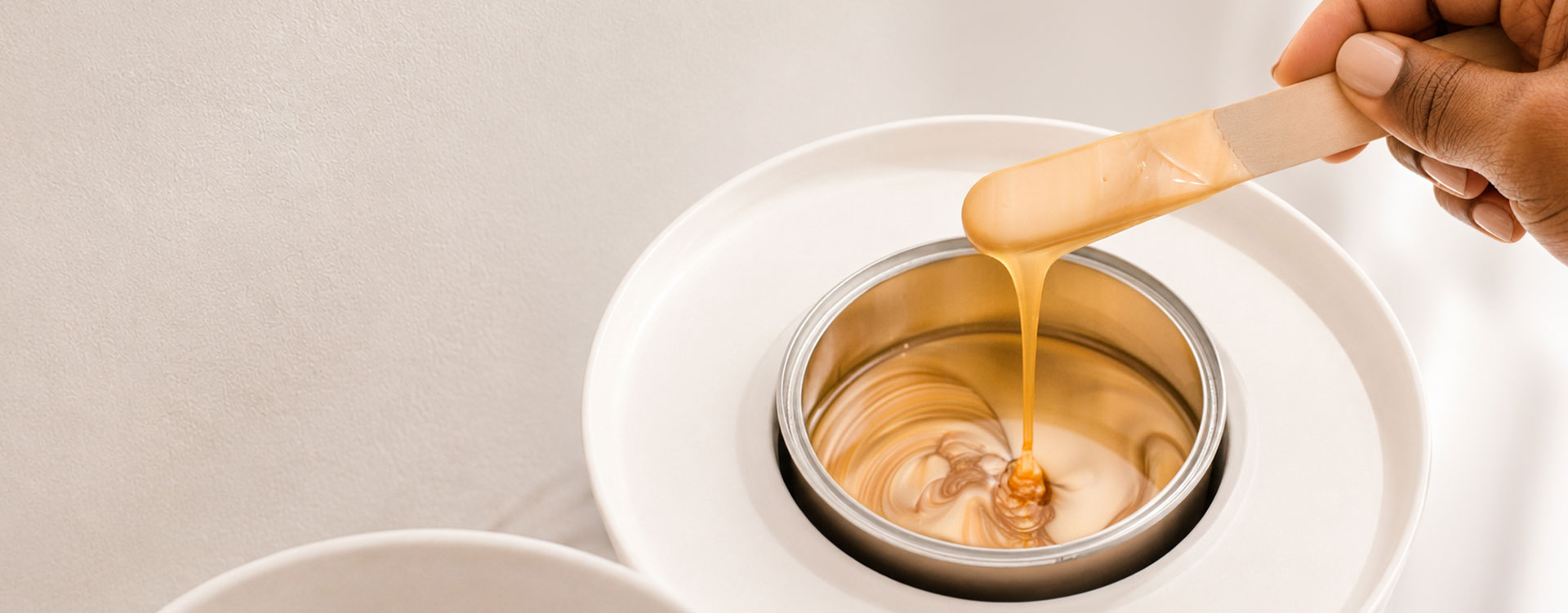 Close-up of amber honey flowing from a wooden spatula into a metal canister inside a white plate.