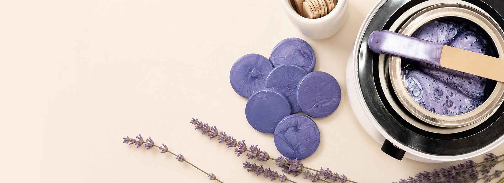 Purple wax melts arranged on a beige surface with lavender sprigs and a nearby wax warmer in the background.