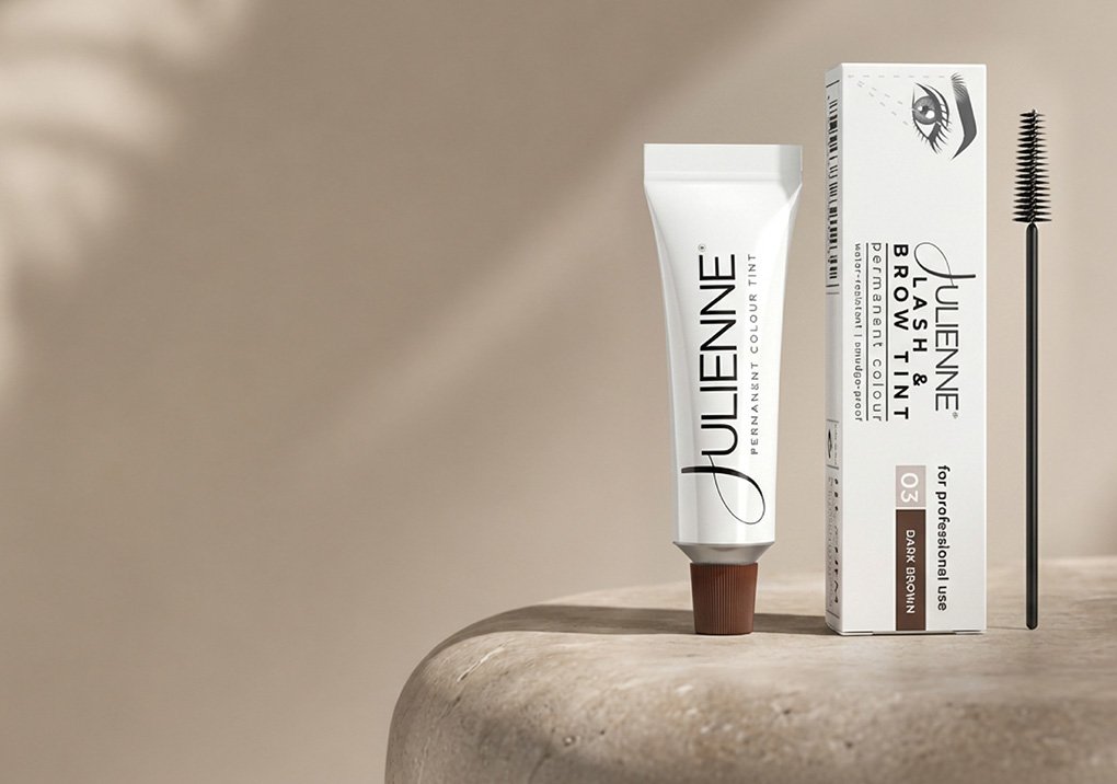 Cosmetic hair color kit: white tube labeled JuLenne permanent colour tint beside its boxed packaging and an applicator wand on a beige surface