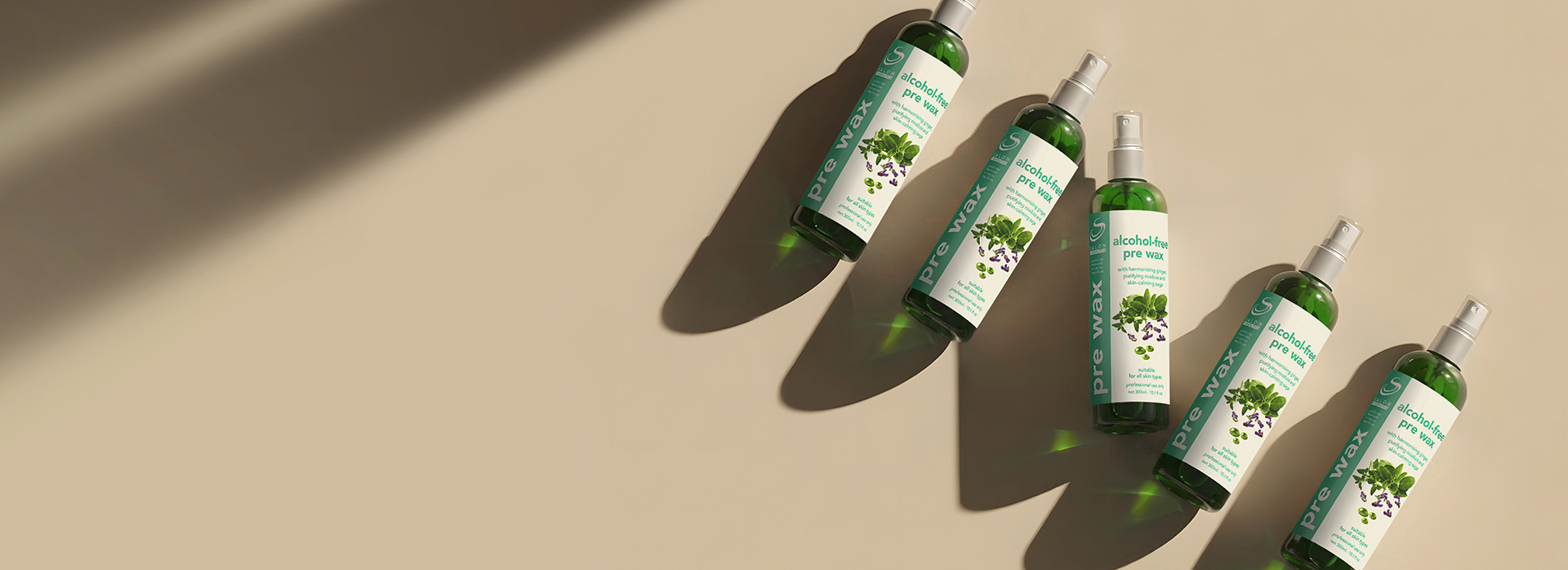 Row of green bottles labeled 'alcohol-free pre-wax' arranged diagonally on a beige background with long shadows