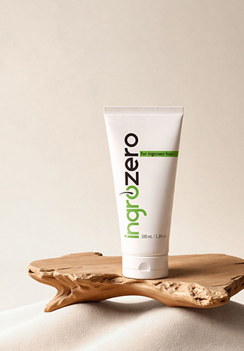 White tube labeled 'ingrow zero' with a green accent sits on a light wooden pedestal, indicating a skincare product for ingrown hair (100 ml).