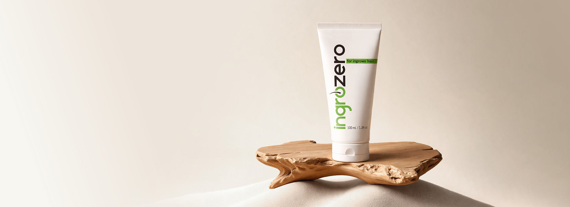 White tube of ingrozero skincare for ingrown hair displayed on a natural wooden stand.
