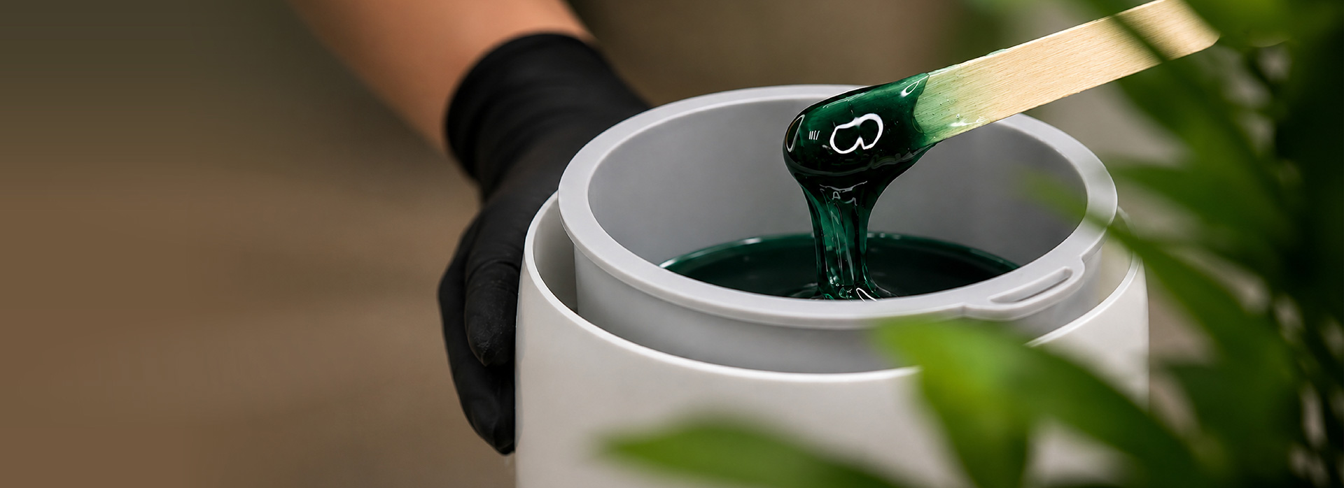 Gloved hand pouring thick green resin from a spatula into a white container during a crafting process