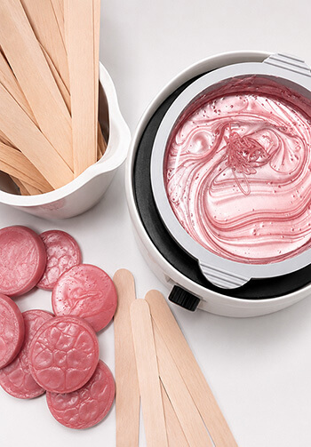 Top-down view of a white fondue pot with pink chocolate, surrounded by a cup of wooden sticks and pink cookies on a white surface.
