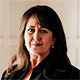 Portrait of a woman with long dark hair wearing a black jacket, looking at the camera indoors.